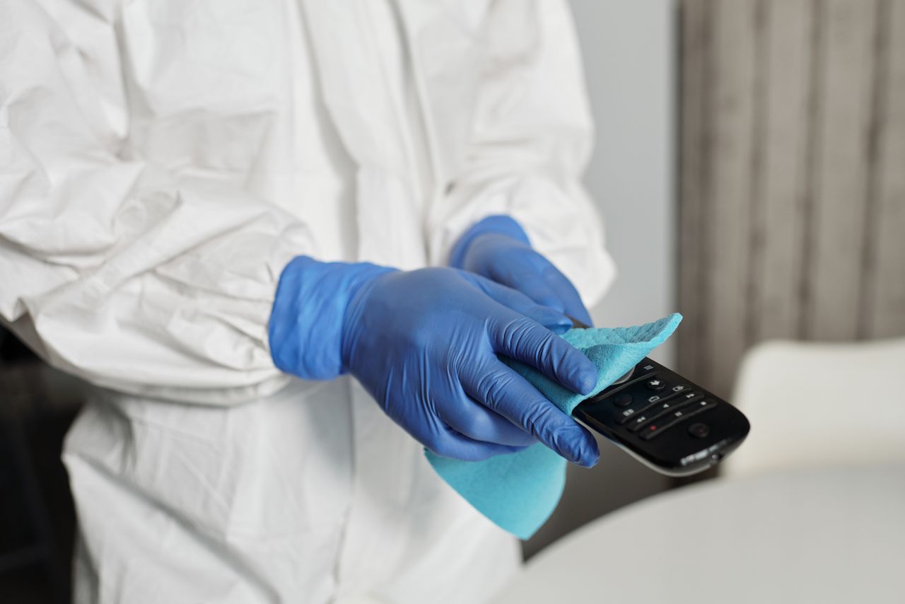 Close-up showing a person sanitizing a remote control while wearing protective gloves to keep it clean.