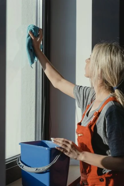Individual in full protective gear holding disinfectant spray and gloves indoors for safety.